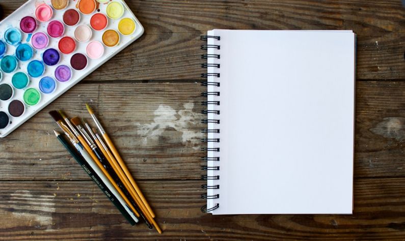 Portfolio Creative - paint brushes next to drawing book and water color palette
