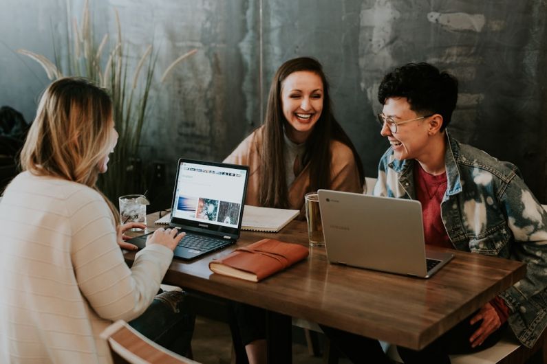 Work Culture - three people sitting in front of table laughing together